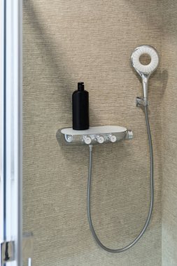 Duş kabini. Dekoratif bej duvar ve duş başlığı. Siyah şampuan şişesi. Modern banyo tasarımı. Dikey çerçevelenmiş çekim.