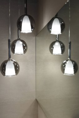 Tavan lambası. Modern üç lamba avizesi. Banyoda lamba var. Aynaya yansıyor. Dikey çerçevelenmiş çekim.