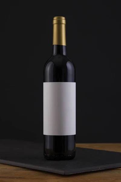 Botella aislada de vino tinto en negro, fondo de madera y etiqueta blanca — Foto de Stock