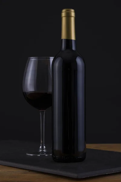 Botella aislada de vino tinto en negro, fondo de madera y sin etiqueta — Foto de Stock