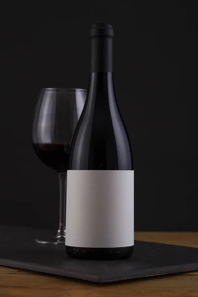 Botella aislada de vino tinto en negro, fondo de madera y etiqueta blanca — Foto de Stock