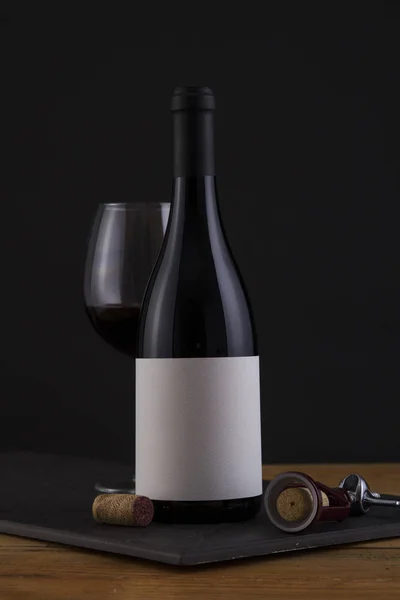 Botella aislada de vino tinto en negro, fondo de madera y etiqueta blanca — Foto de Stock