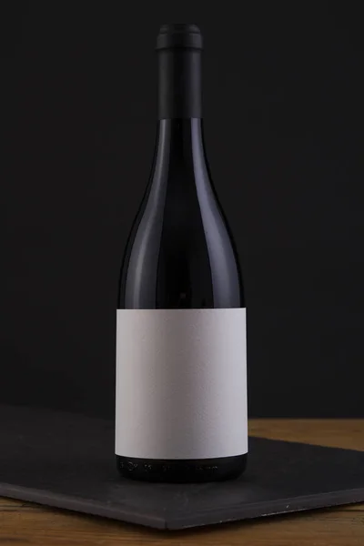 Botella aislada de vino tinto en negro, fondo de madera y etiqueta blanca — Foto de Stock