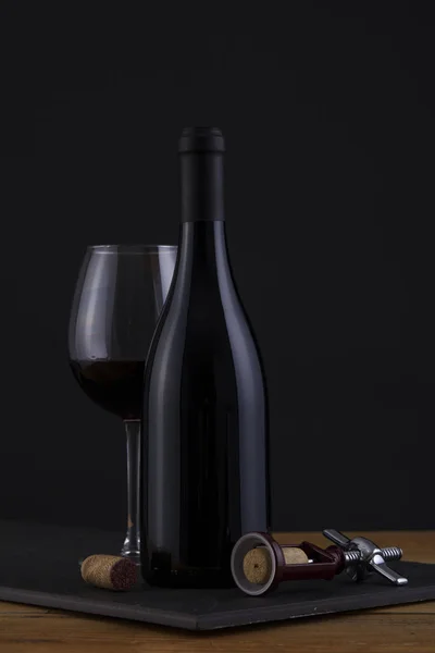 Botella aislada de vino tinto en negro, fondo de madera y etiqueta y vidrio negro — Foto de Stock