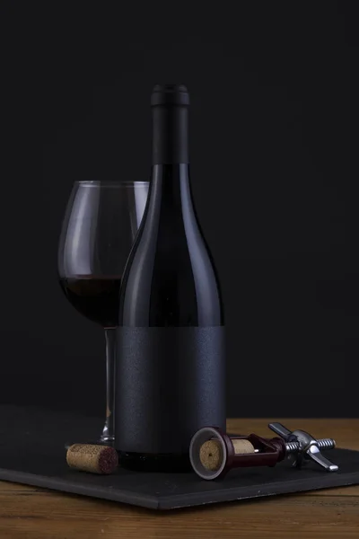 Botella aislada de vino tinto en negro, fondo de madera y etiqueta y vidrio negro — Foto de Stock