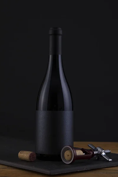 Botella aislada de vino tinto en negro, fondo de madera y etiqueta negra — Foto de Stock