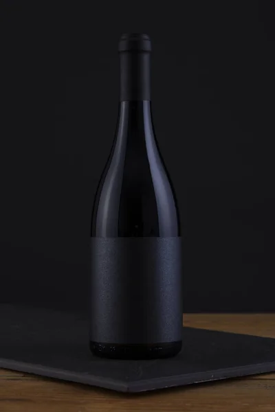 Botella aislada de vino tinto en negro, fondo de madera y etiqueta negra — Foto de Stock