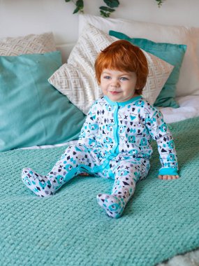 Komik Kızıl saçlı çocuk yatağa oturmuş ve gülümseyen pijama