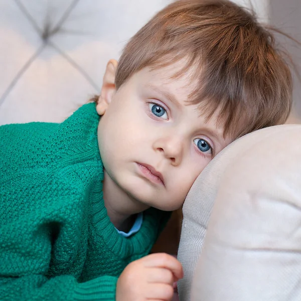 Beautiful blue-eyed boy lying on the couch and looking sad look — Stock Photo, Image