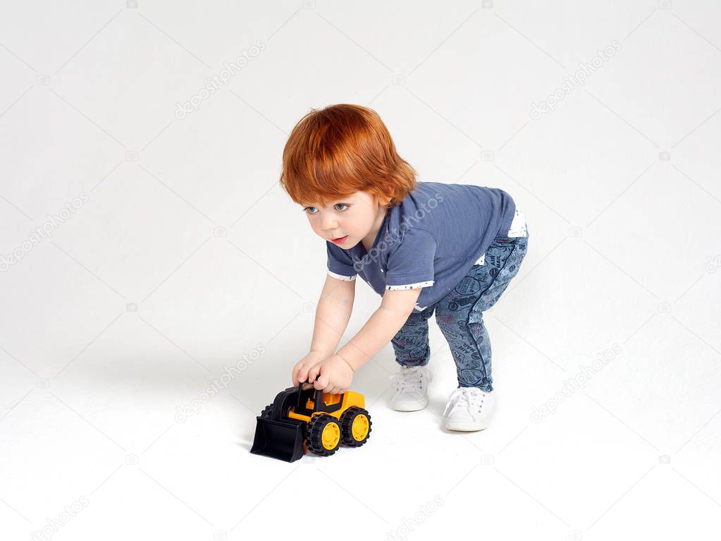 Red-haired little boy playing with yellow toy tractor