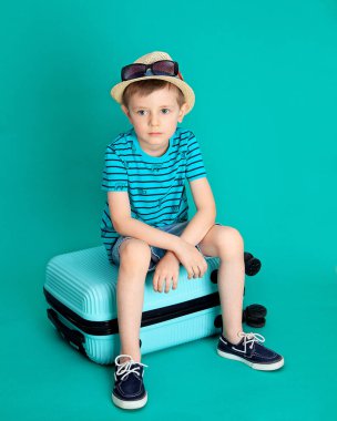 Şapkalı çocuk mavi bir bavula oturur, yolculuğa çıkar ve üzülür.