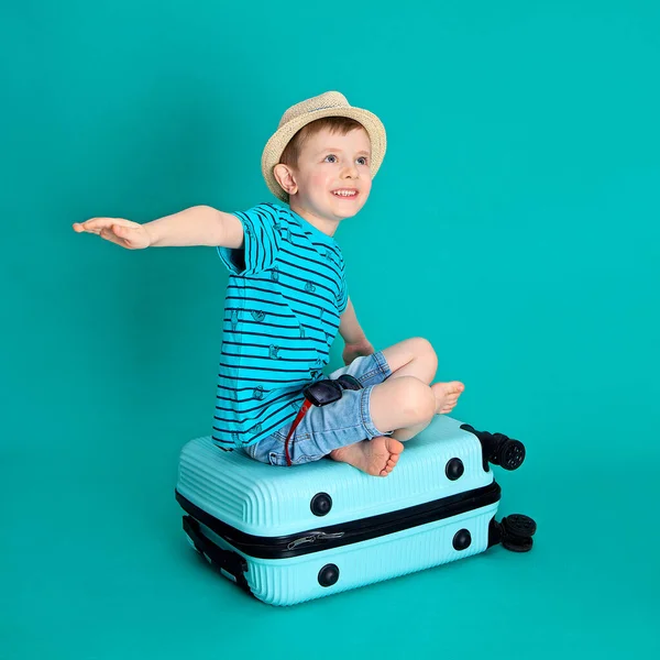Chłopiec Kapeluszu Siedzi Niebieskiej Walizce Przedstawia Samolot Kolorowym Tle — Zdjęcie stockowe