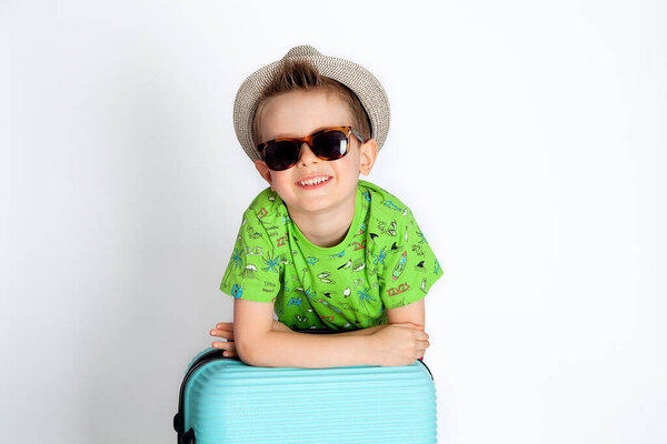 boy traveler in glasses and hat leans on a suitcase and smiles