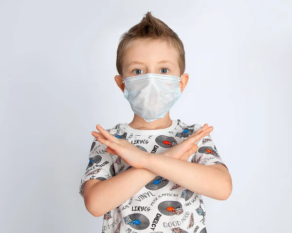 blue-eyed boy in a medical mask against coronovirus shows stop on a white background