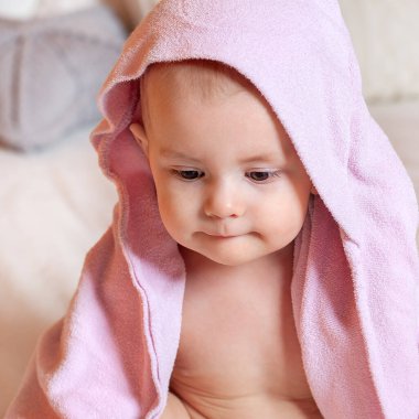 Banyo yaptıktan sonra bir yaşındaki bir bebeğin portresi. Dudakları büzüşmüş güzel bir yüz. Çocuklar için tekstil ve yatak. Pembe banyo havlusu..