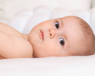 Bebek beyaz bir yatakta yan yatar ve çerçevenin içine bakar. Meraklı ve zeki çocukların gözleri. Büyük bir kız portresi. Annelik bakımı. Aile ve çocuklar. Ebeveynlik ve annelik