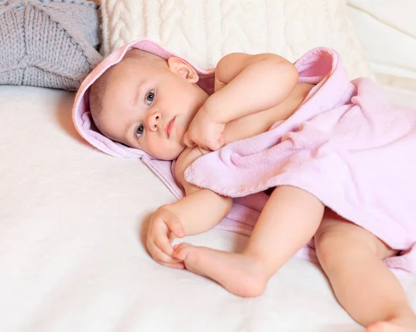 A one-year-old girl lies on her side after bathing and looks sad. She sent me off to get ready for bed. Family and care. Textiles and bedding for children.