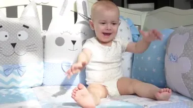 Mavi yataktaki küçük kız gülüyor, gülümsüyor, sallanıyor ve ellerini çırpıyor. Aile ve annelik. Bebeklere bakmak. Komik çocuk. Çocuklar melektir..