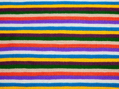 Örülmüş çizgili doku. Yünlü kumaş. Çok renkli süs - kırmızı, sarı, yeşil, mavi, beyaz, kahverengi, turuncu, mor. Örgü, el yapımı. Yakın plan. Atkı, kışlık kıyafetler..