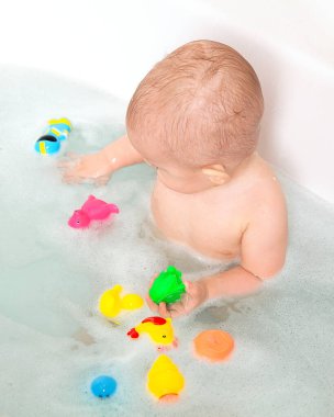 Bebek beyaz bir küvette yıkanır ve renkli lastik banyo oyuncaklarıyla oynar. Cesedin üzerine su damlıyor. Biraz saç. Banyo yapan bebekler, çocuk bakımı, annelik sevgisi ve bakım. Çocuk banyo aksesuarları..