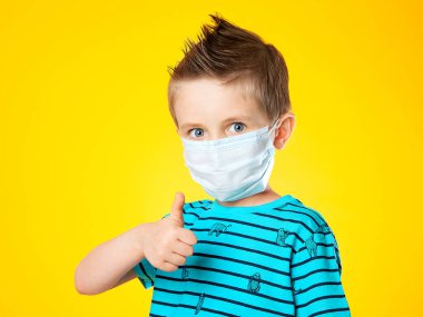 Sarı arka planda tıbbi maske takmış güzel bir Avrupalı çocuğun portresi. Çocuk tabelayı süper gösteriyor, sınıf. Büyük mavi göz. Salgın hastalıklar, salgınlar ve koronovirüsle mücadele..