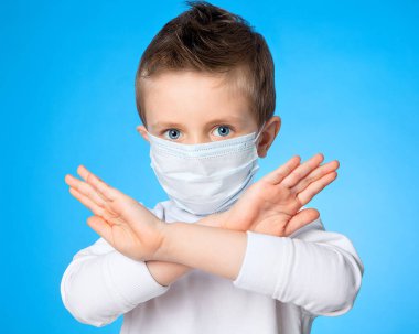 Mavi arka planda tıbbi maske takan beş yaşındaki Avrupalı mavi gözlü çocuk durduğunu gösteriyor. Endişe, enfeksiyon tehlikesi. Salgına karşı mücadele, salgın virüsü. Covid 19.