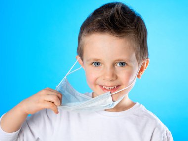 Güzel bir Avrupalı çocuk tıbbi maskesini çıkarıp gülüyor ve mutlu oluyor. Çocuk çok mutlu. Coronavirus 'a karşı zafer. Salgının sonu, Covid-19 salgını. Nekahat dönemi.