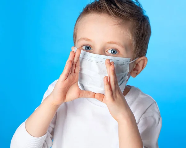 A boy in a medical mask screams and puts his hands to his mouth. On a blue background. Prevention of coronavirus infection. The fight against the epidemic, the pandemic Covid-19.