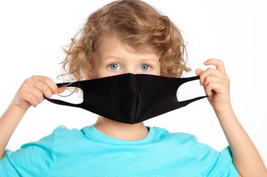 Kıvırcık, mavi gözlü, Coronavirus 'a karşı koruyucu maske takan sarışın bir çocuk. Beyaz arka planda siyah maske. Covid-19 salgınıyla savaşmak, bir salgın. Soğuk algınlığı ve gribi önleme.