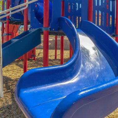 Kare, güneşli bir günde evlere ve gökyüzüne karşı parktaki parlak mavi kaydırağa odaklan.