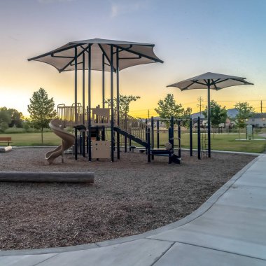 Kare çerçeve, günbatımında ağaçlı evler ve mavi gökyüzü arkaplanlı mahalle parkı