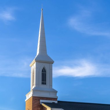Kare çerçeve, kilise kulesiyle ve mavi gökyüzüne karşı kırmızı tuğla duvarla çevrili.