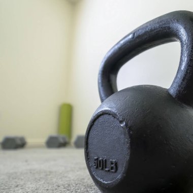 Kare çerçeve Halı döşemeli ve beyaz duvarlı bir spor salonundaki siyah kettlebell 'i kapat
