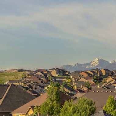 Kare çerçeve, önü ağaçlarla ve evlerle kaplı karla kaplı bir dağın çarpıcı manzarası.