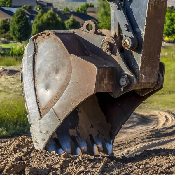 Square frame Focus on the bucket and arm of an excavator digging soil at a construction site — Stock Photo, Image