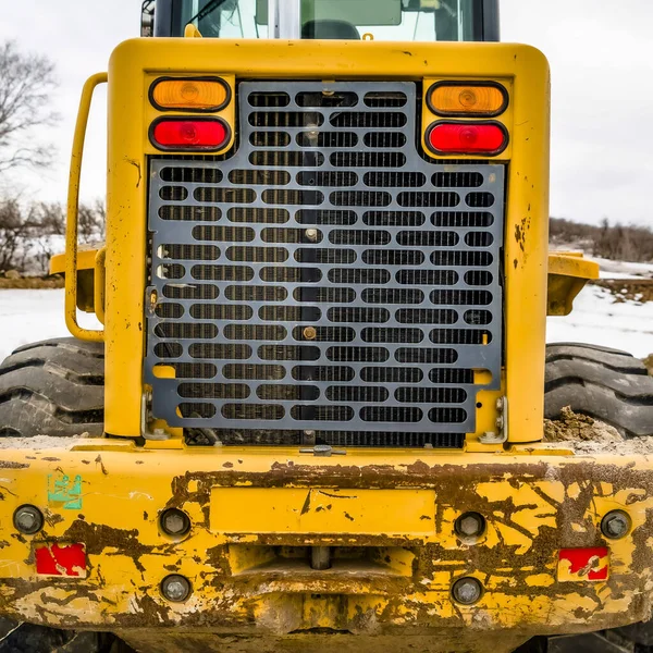 Square Focus on the back of a old yellow bulldozer against snowy ground and cloudy sky — Zdjęcie stockowe