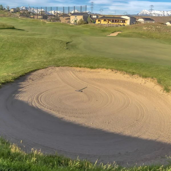 Quadratische Nahaufnahme einer Sandfalle an einem sonnigen Golfplatz mit Häusern in der Ferne — Stockfoto