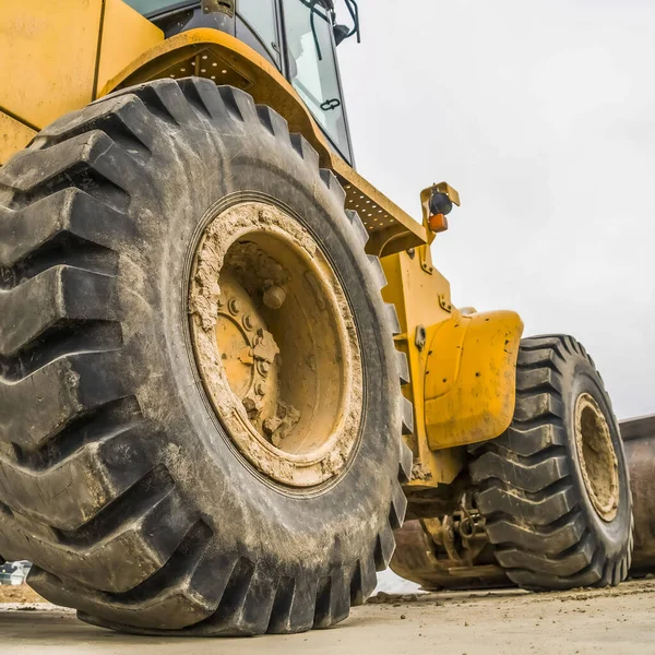 Quadratischer Rahmen konzentriert sich auf die schwarzen Gummiräder einer gelben Planierraupe auf einer Baustelle — Stockfoto