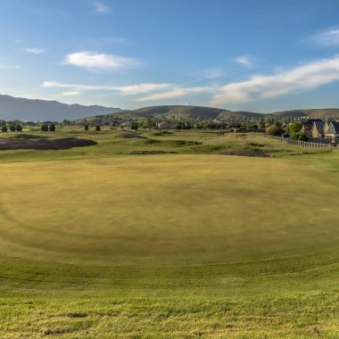 Evlere, dağlara, gökyüzüne ve bulutlara karşı kare çerçeveli golf sahası