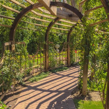 Kare çerçeveli ahşap çarşaf, yemyeşil bitkiler ve taş tuğla yolu olan bir düğün yerinde.