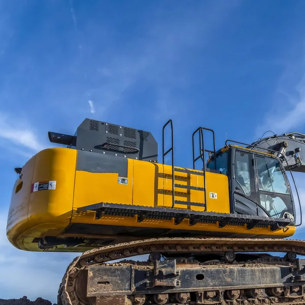 Quadratischer gelber Bagger mit durchgehenden Gleisen gräbt Erde auf einer Baustelle — Stockfoto