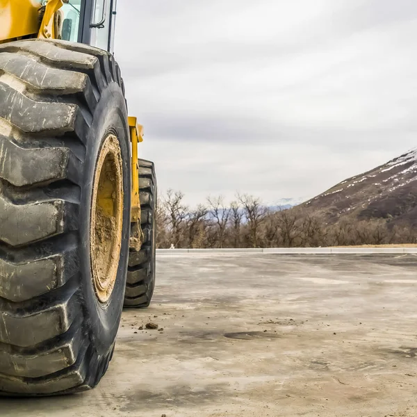 Square Close up of the tires of a bulldozer against snow peaked mountain and cloudy sky — Stock fotografie