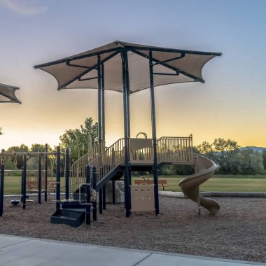 Gün batımında izlenen bir çocuk parkında Kare Kaydırak ve şemsiyelerle tırmanma