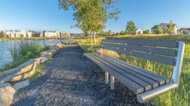Güneşli bir günde, arka planda evler ve binalar olan bir gölün kıyısındaki Bench 'in manzarası.