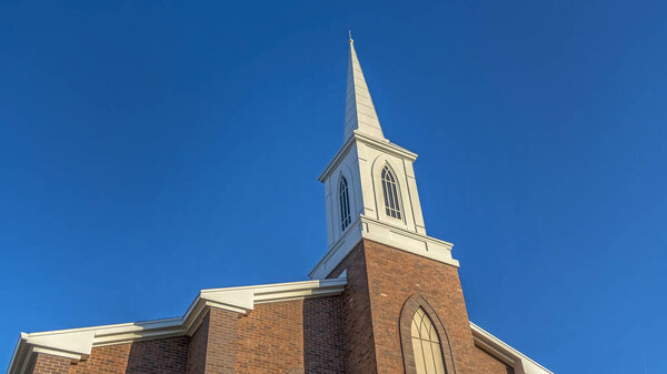 Panorama Church with classic red brick exterior wall and white steeple against blue sky