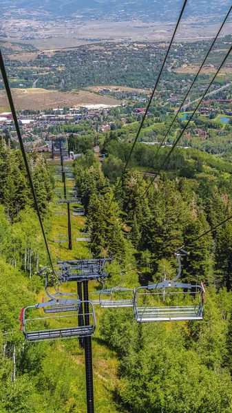 Verticaal frame Stoelen liften over wandelpaden en bomen op de berg met gebouwen in Park City — Stockfoto