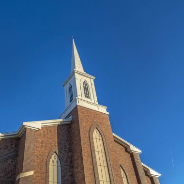 Klasik kırmızı tuğlalı dış duvarı ve mavi gökyüzüne karşı beyaz çan kulesi olan kare çerçeve kilisesi.