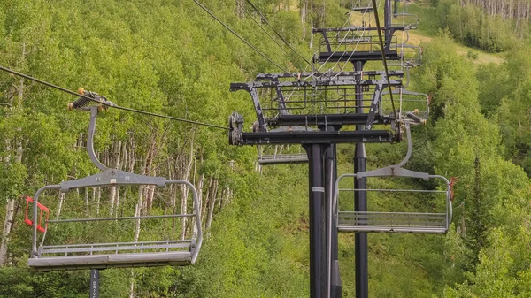 Panorama frame Stoeltjesliften op kabels over skiberg met dikke groene bomen in het laagseizoen — Stockfoto