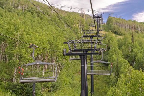 Καρέκλες σε καλώδια πάνω από βουνό σκι με πυκνά πράσινα δέντρα κατά τη διάρκεια της εκτός εποχής — Φωτογραφία Αρχείου