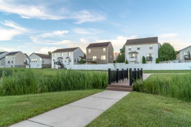 Çimenli bir zeminde, arka planda evleri olan göl ve patikalar üzerinde köprü.